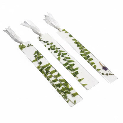The J.M Press clear bookmarks with pressed green fern leaves and a small purple flower, tied with white ribbon.