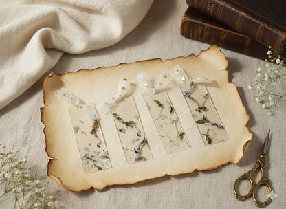 The J.M Press Collection of four clear resin bookmarks with real pressed flowers and leaves, each with a white ribbon tie.